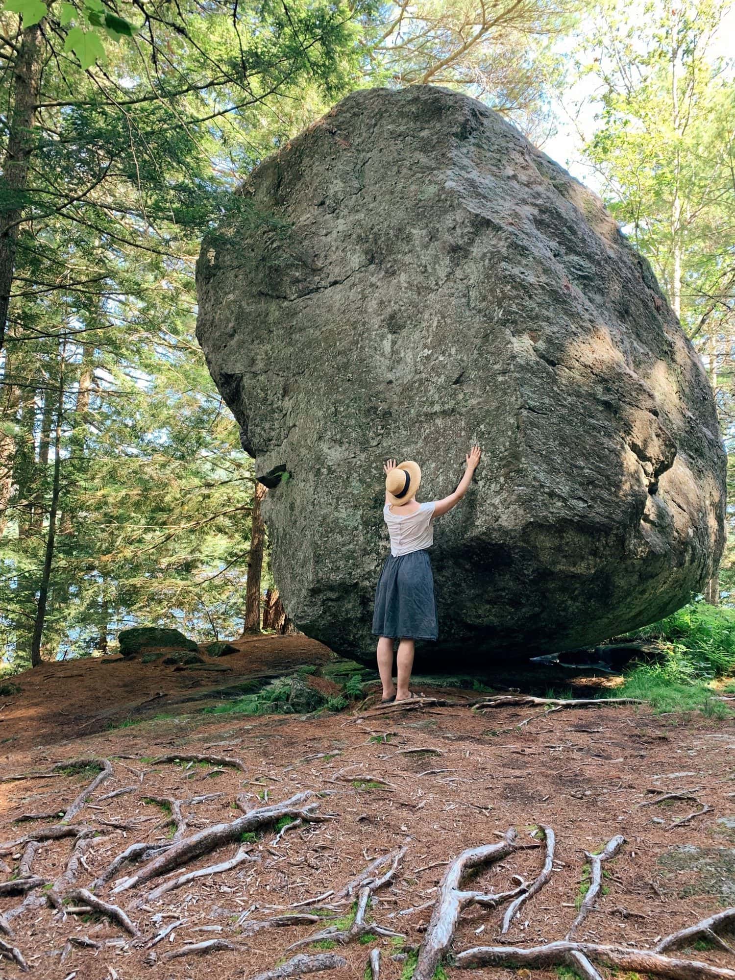 Woman touching a giant rock balanced in a forest